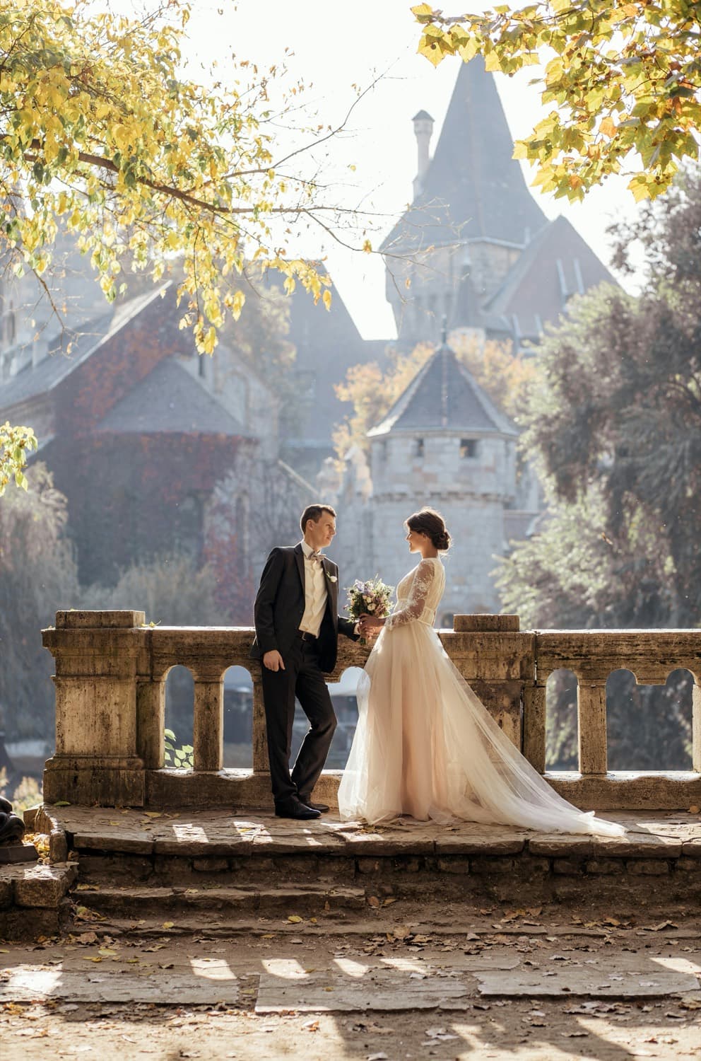 A couple on a stone balustrade in autumn light, a turreted house behind them