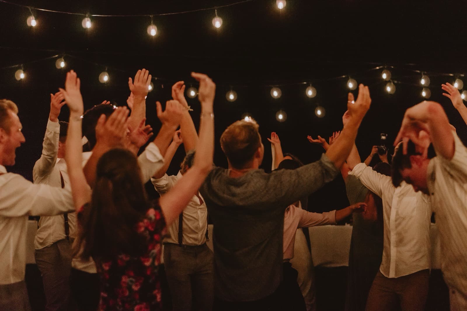 Guests dancing with their arms raised under string lights after dark