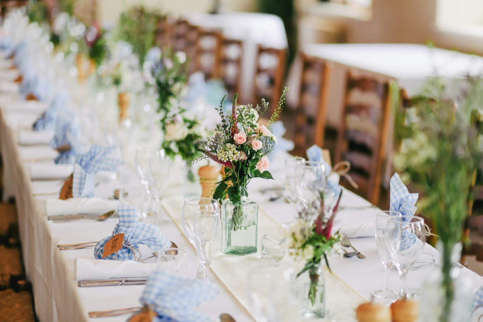 A long banquet table laid with wildflowers, blue linen napkins and glassware